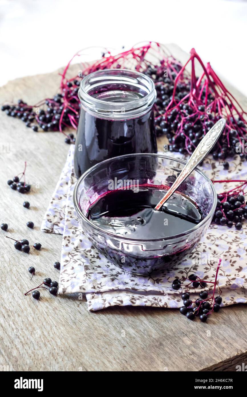 Sciroppo di sambuco nero fatto in casa in recipiente di vetro e vaso e mazzi di sambuco nero sullo sfondo Foto Stock