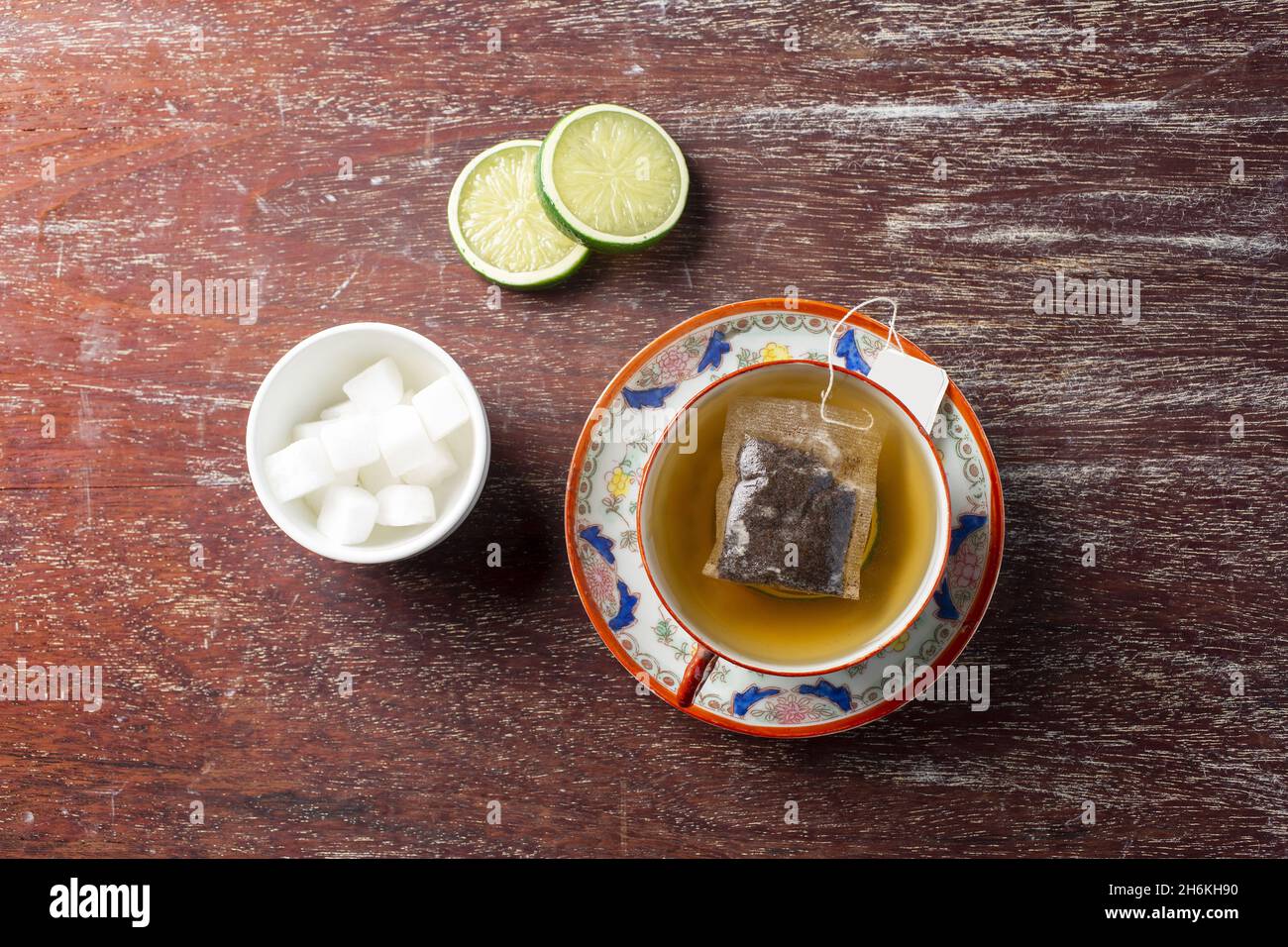 Vista dall'alto di un teabag in una tazza piena, due fette di lime e una piccola ciotola bianca con cubetti di zucchero Foto Stock