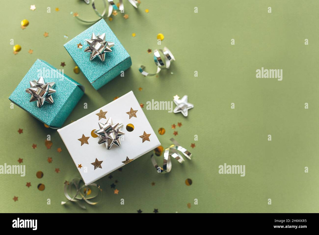 Scatole regalo bianche e verdi con un tinsel e confetti su sfondo verde. Il concetto di un regalo, un nuovo anno, un background festivo. Disposizione piatta, vista dall'alto Foto Stock