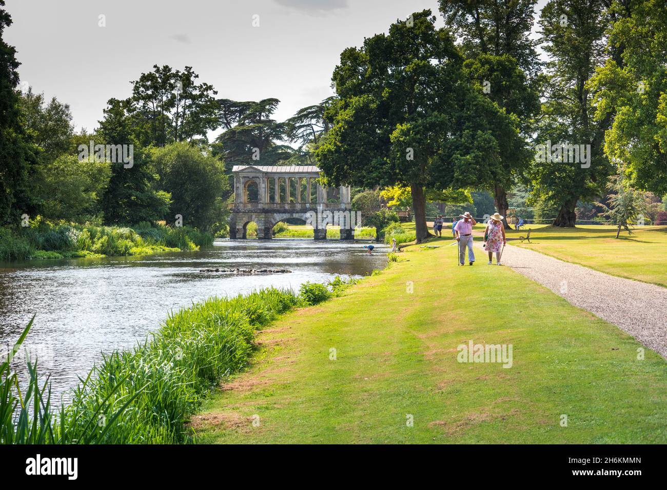 Coppia anziana che cammina accanto al fiume Nadder con i giardini del Ponte Palladian e il parco a Wilton House Wilton Inghilterra Foto Stock