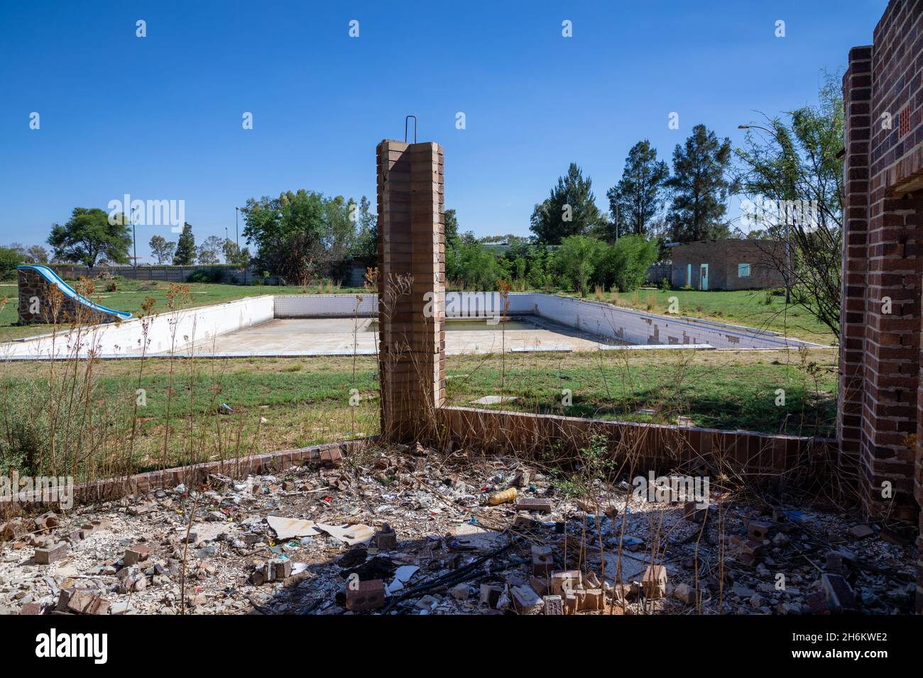 Piscina abbandonata con un pezzo di muro di mattoni rotto di fronte ad essa. Foto Stock