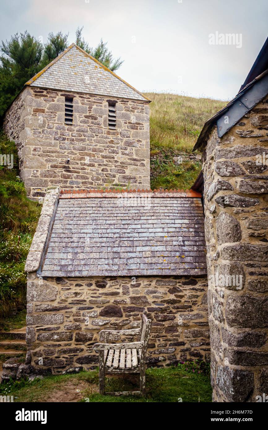 La chiesa di St Winwaloe e la panchina intemprata della Gunwalloe's Church Cove, in Cornovaglia, mostrate in luce soffusa, evidenziano le consistenze rustiche e il carattere costiero Foto Stock