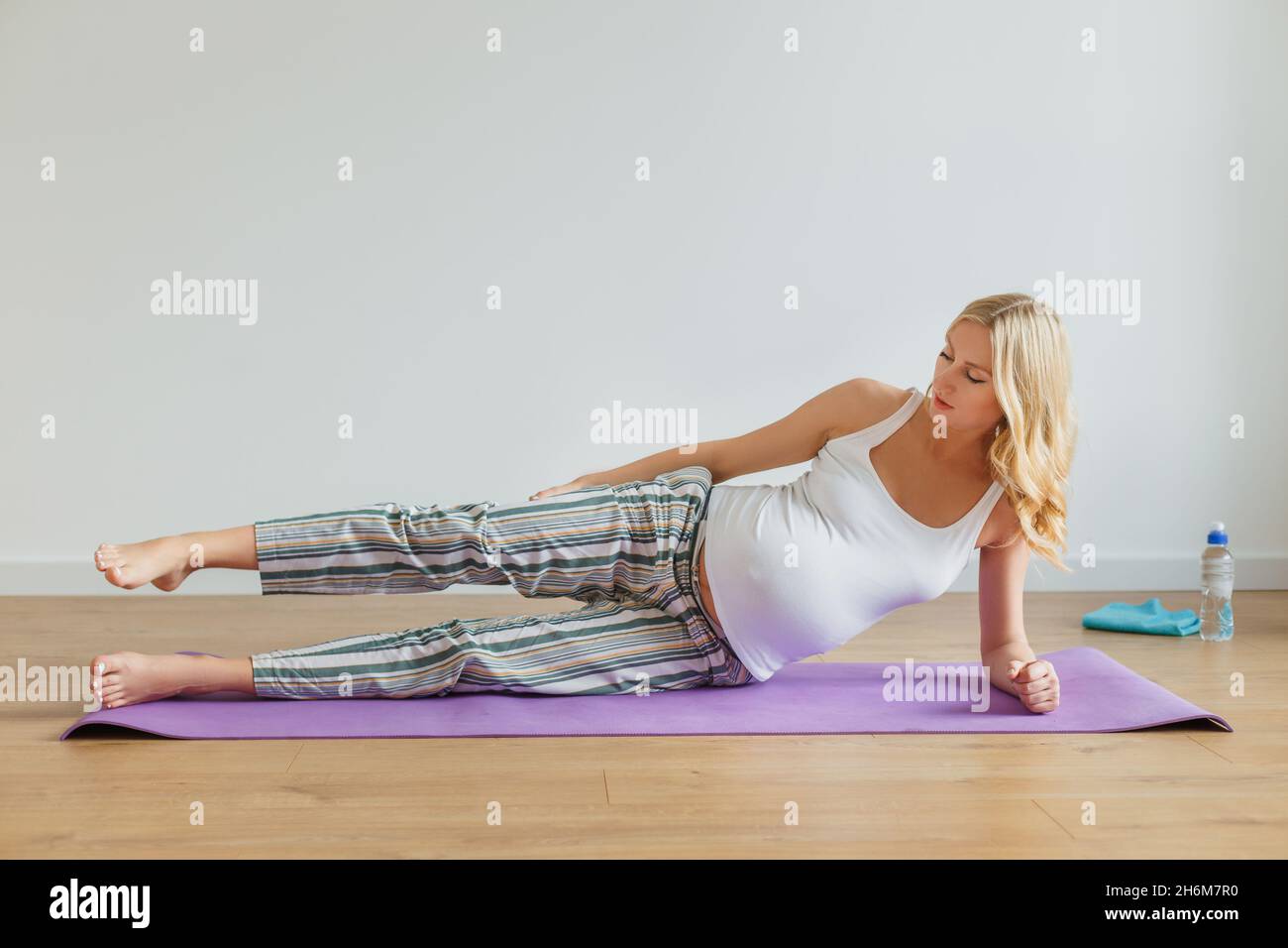 Donna bionda incinta che fa yoga prenatale a casa. Futura madre che ha un certo esercizio per le gambe su tappeto viola. Concetto di salute e cura del corpo, fitness Foto Stock