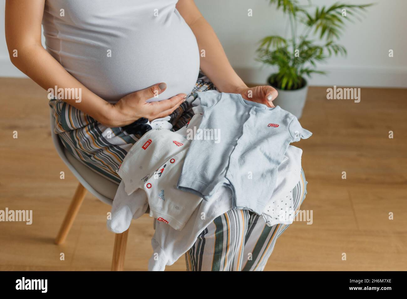Donna bionda incinta che guarda sui piccoli vestiti per il suo bambino. Felice futuro madre tenuta in mani cute bodywear per neonato. Concetto di genitorialità Foto Stock