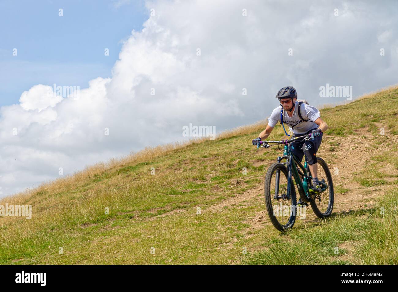 Ciclista non identificato che percorre una collina erbosa sotto le spettacolari nuvole estive delle Malvern Hills, Worcestershire, Inghilterra, Regno Unito. Foto Stock