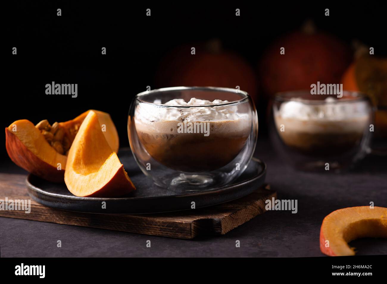 Tazza di latte di zucca speziato con panna montata e fette di zucca su sfondo di legno scuro. Foto Stock