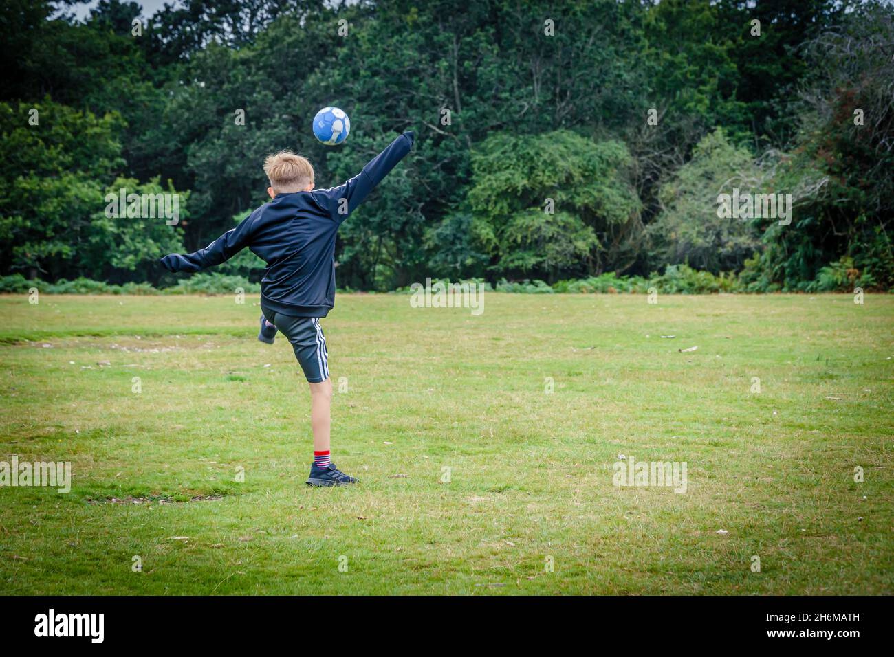 Ragazzo caucasico di 9 anni che gioca a calcio in un campo, New Forest, Hampshire, Regno Unito Foto Stock