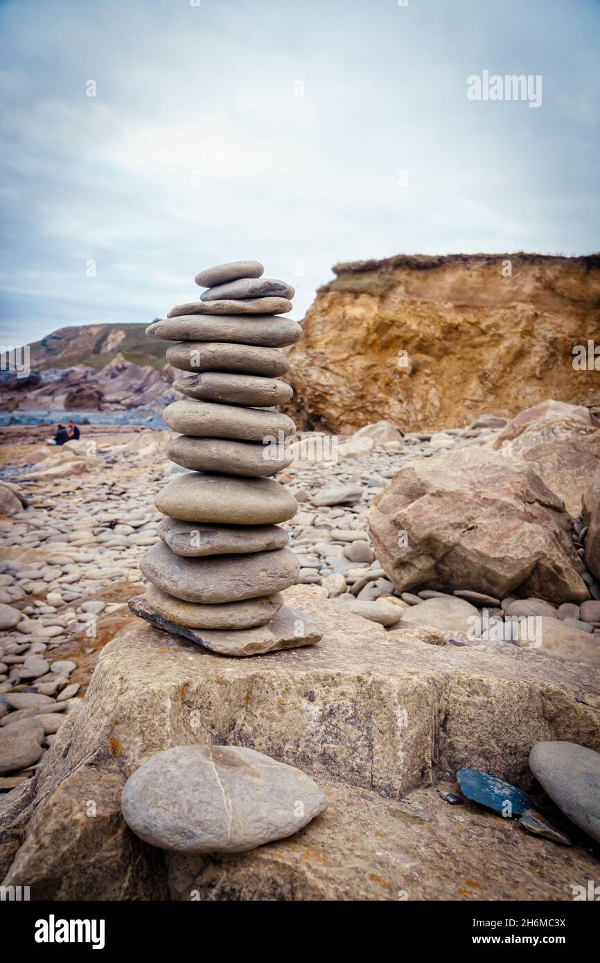 Ciottoli lisci impilati e bilanciati sulle rocce della spiaggia di Dollar Cove, Gunwalloe, Cornovaglia, Inghilterra, sotto un cielo coperto con aspre scogliere alle spalle. Foto Stock