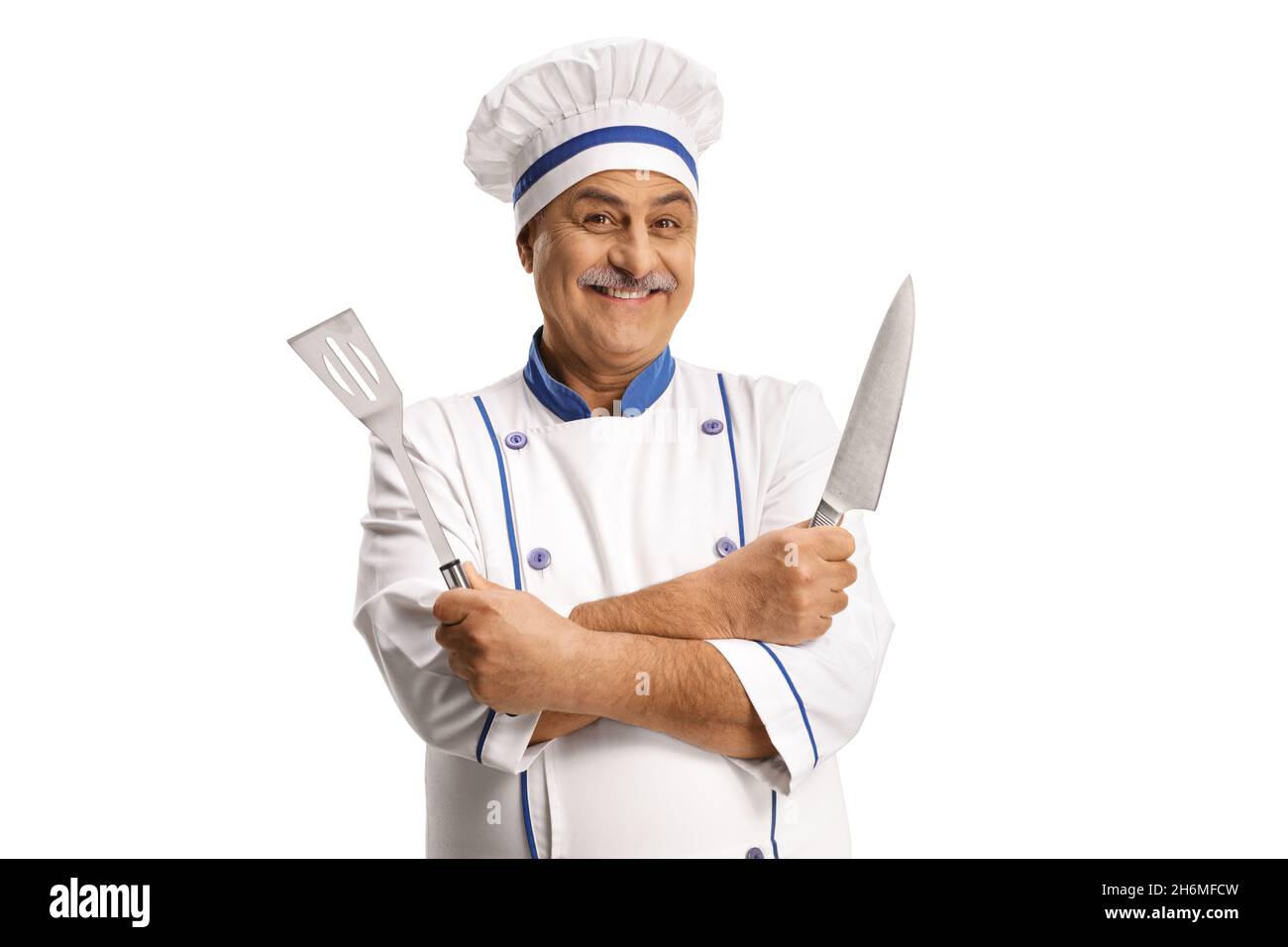 Allegro chef maschio maturo che tiene un coltello affilato e un utensil Turner isolato su sfondo bianco Foto Stock