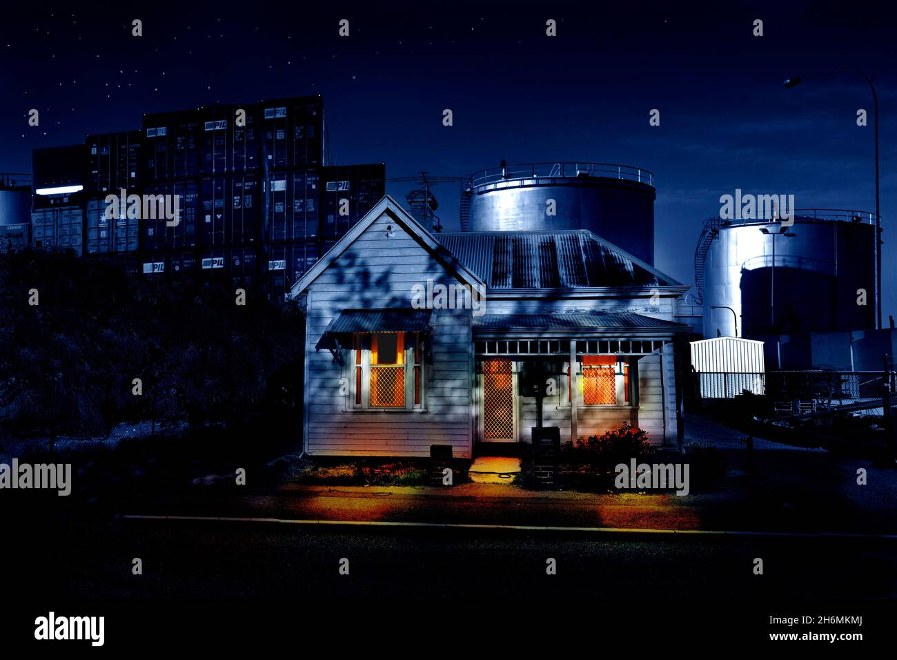Una vista crepuscolo della casa di legno che lentamente è circondata da un porto commerciale, serbatoi di deposito e contenitori orlo la casa in. Foto Stock