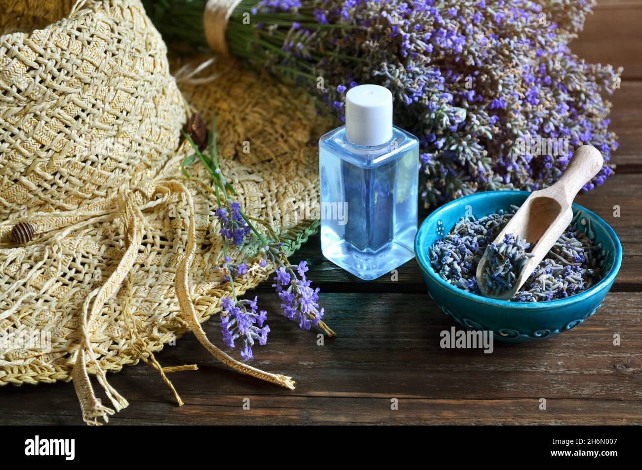 Cappello estivo in vimini con fiori freschi e secchi di lavanda e bottiglia di olio essenziale o acqua di lavanda per la produzione di cosmetici naturali. Foto Stock