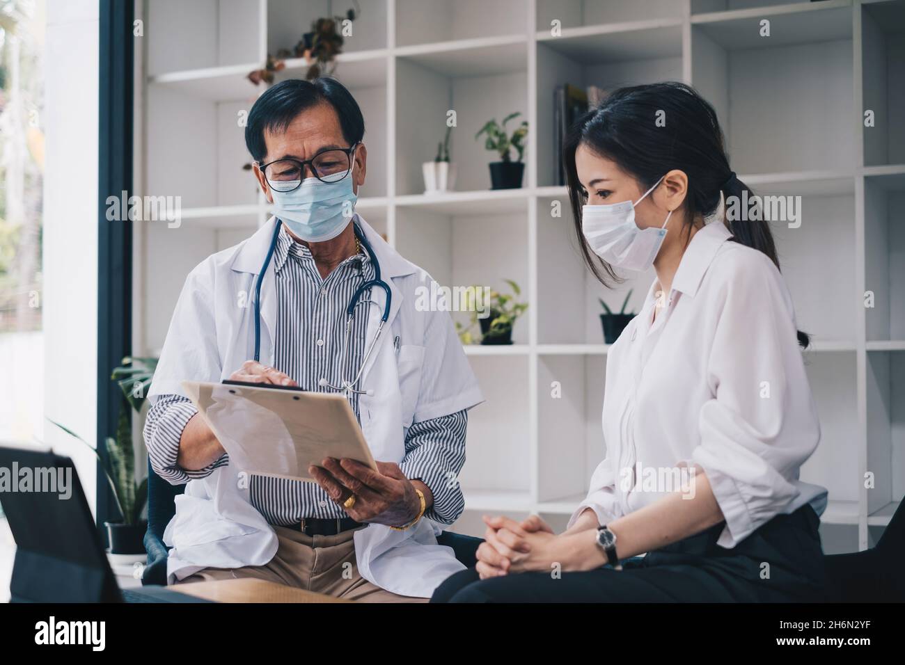 Una donna con maschera cerca consigli medici sulla sua salute e piani futuri. Dottore con maschera spiegare il concetto sanitario e medico. Foto Stock