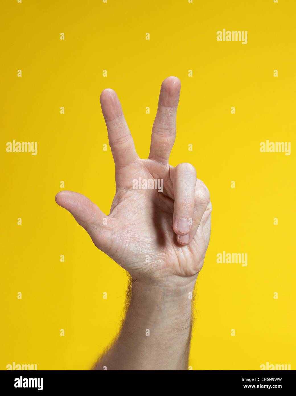 Primo piano del gesto della mano maschile su sfondo giallo. Man mano isolato mostrando tre dita. Foto Stock
