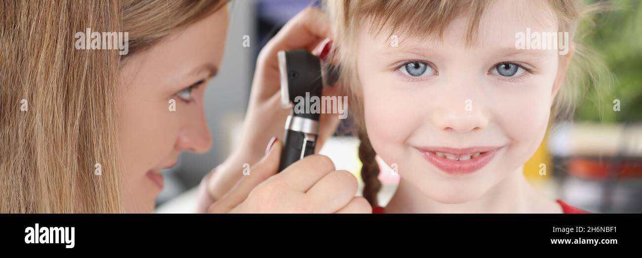 Donna pediatra che guarda il timpano di bambina usando otoscopio in clinica Foto Stock