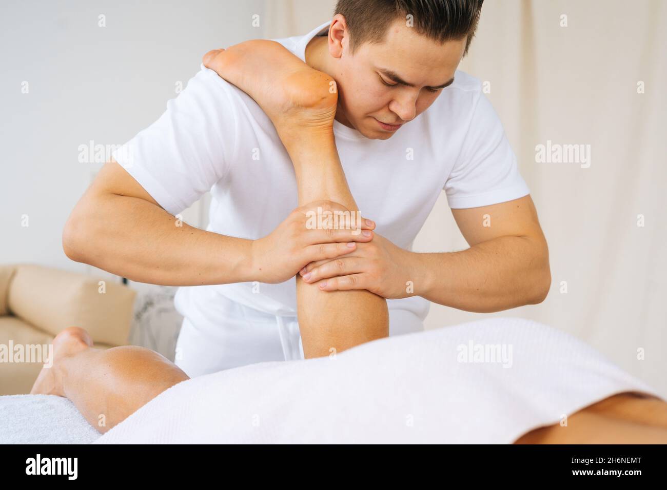 Primo piano viso maschile professionale con mani forti massaggiando i muscoli del polpaccio sulla gamba inferiore dell'atleta muscolare dopo l'allenamento sportivo fisico Foto Stock