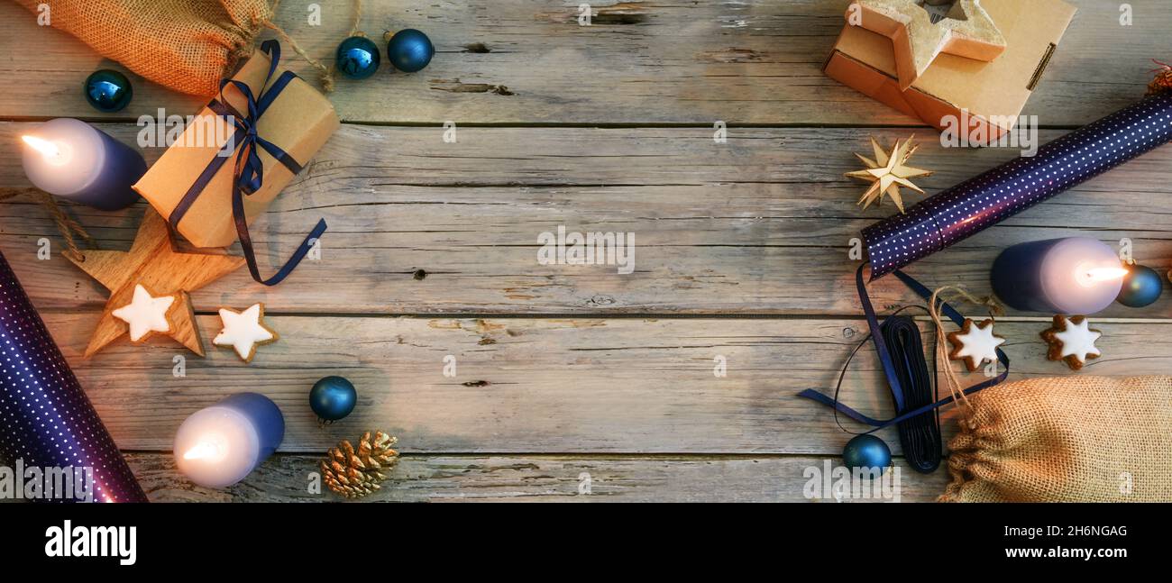 Preparazione di Natale sfondo, confezione regalo con carta naturale e blu, baubles, stelle e candele accese come decorazione, rustico tavolo in legno con c Foto Stock
