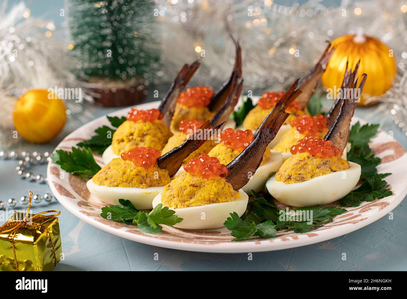 Uova farcite con spratti e caviale rosso su un piatto su sfondo blu. Delizioso spuntino festivo Foto Stock