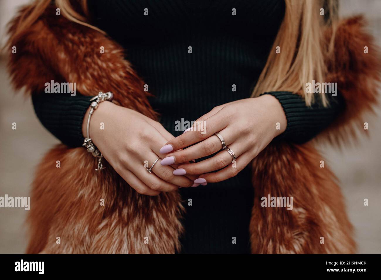 Mani femminili con manicure rosa, braccialetto argento e anelli. Figura femminile ritagliata con giubbotto marrone in pelliccia Foto Stock