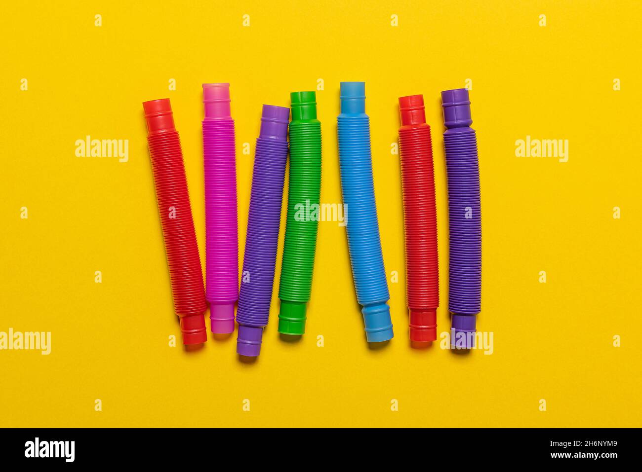 Fila di pochi nuovi giocattoli per bambini a tubo pop rosso, blu, rosa, verde e giallo. Set di allegre tubi multicolore antistress in plastica su br Foto Stock