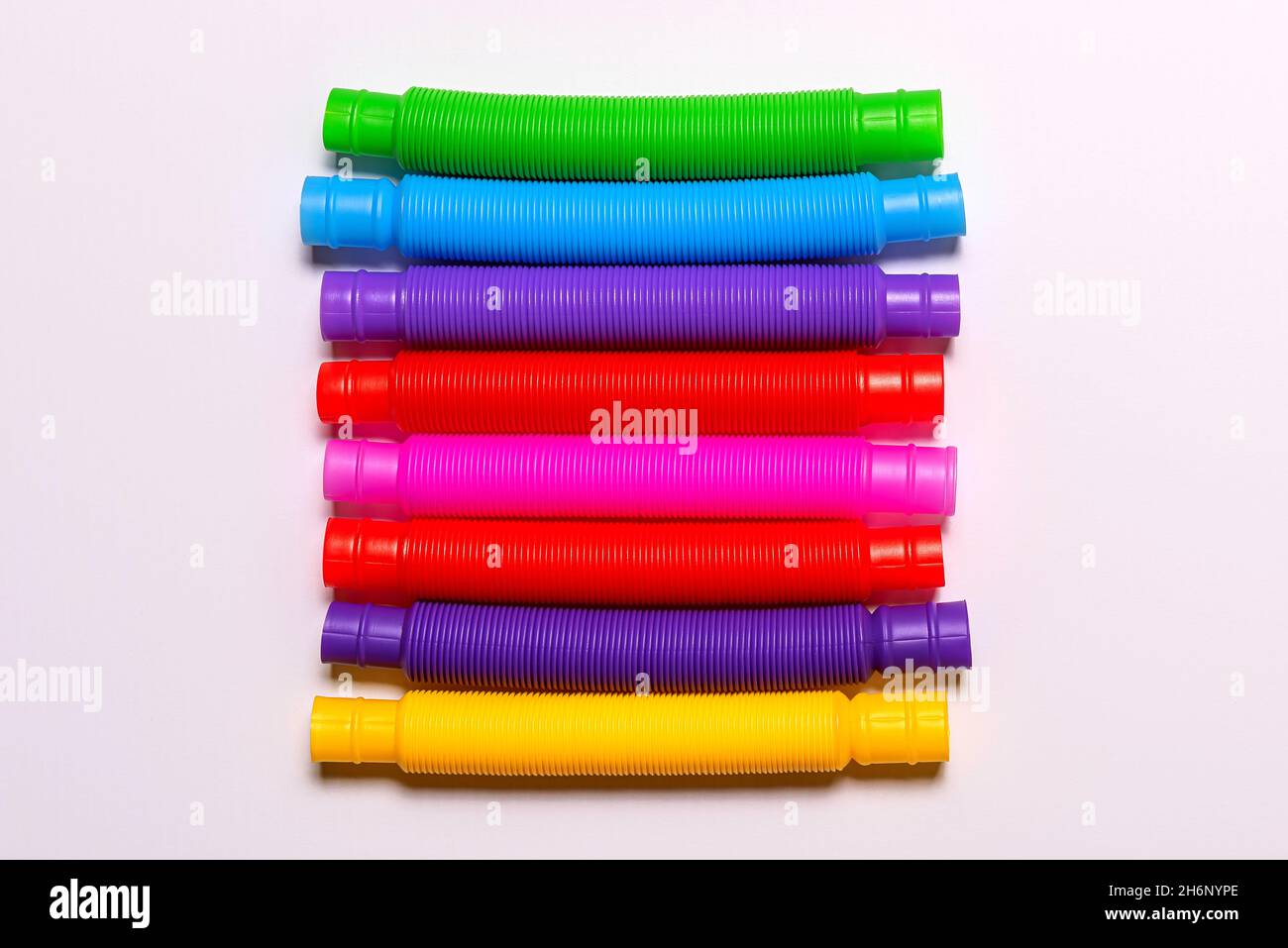 Primo piano di alcuni nuovi giocattoli per bambini a tubo pop rosso, blu, rosa, verde e giallo. Fila di allegro plastica antistress multicolore tubi Foto Stock