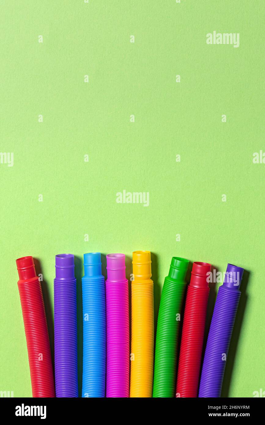 Piatto con fila di pochi colorati rosso, blu, rosa, verde e giallo tubo anti-stress bambini giocattoli. Set di tubi multicolore in plastica su gre luminoso Foto Stock
