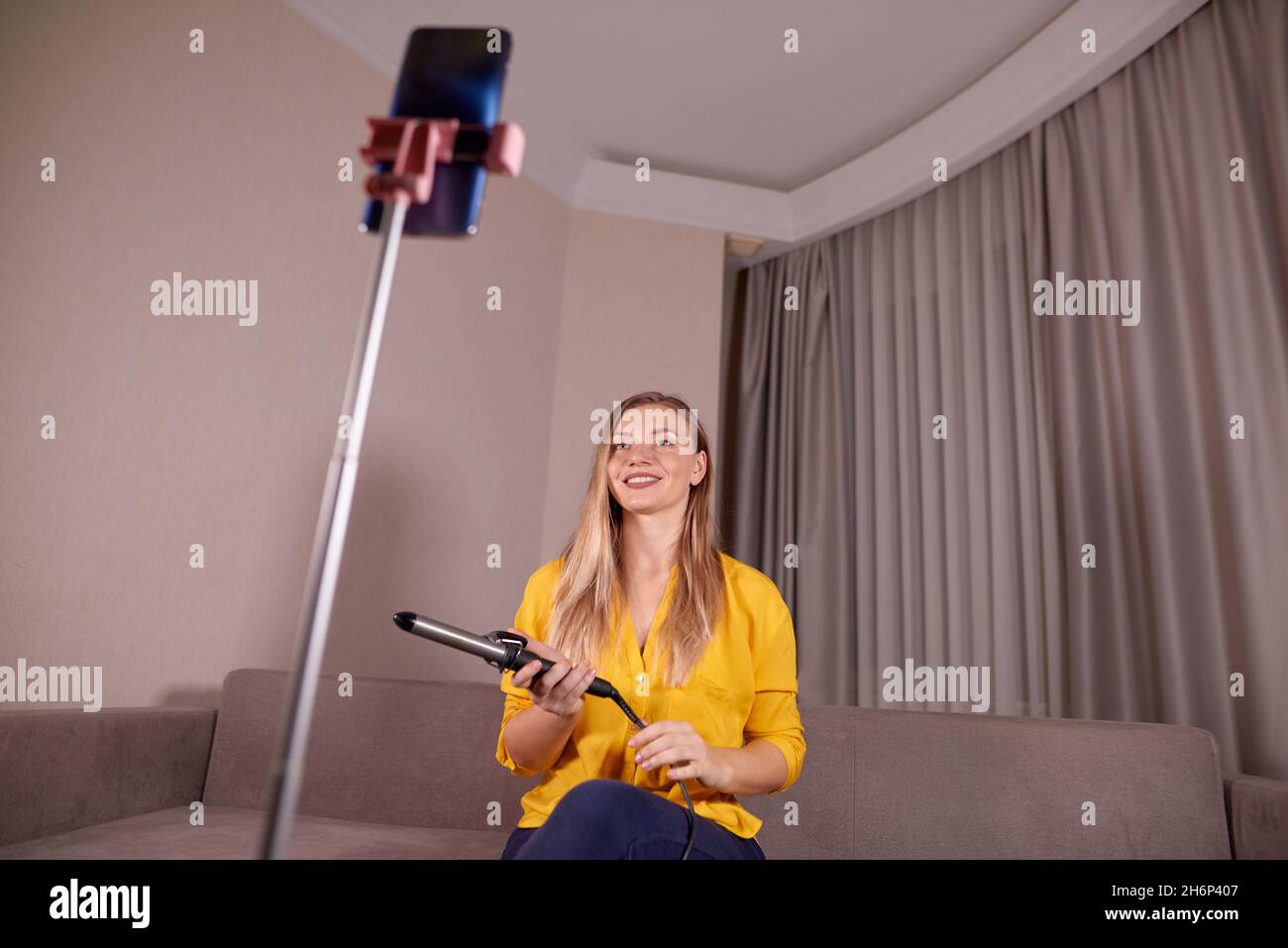 bella donna tenere arricciacapelli ferro e registra online formazione come fare rapidamente e facilmente styling a casa Foto Stock