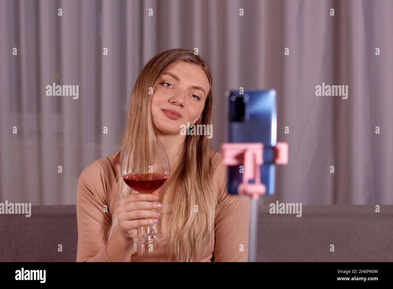 Giovane bella donna che ha alla videochiamata notturna, con smartphone, seduta sul divano, bere vino rosso. Concetto di relazione a lunga distanza Foto Stock