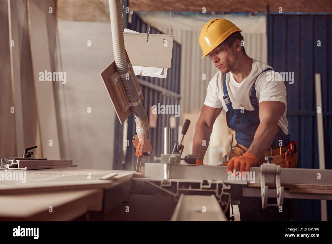 Costruttore maschile serio che utilizza la macchina per la lavorazione del legno in officina Foto Stock