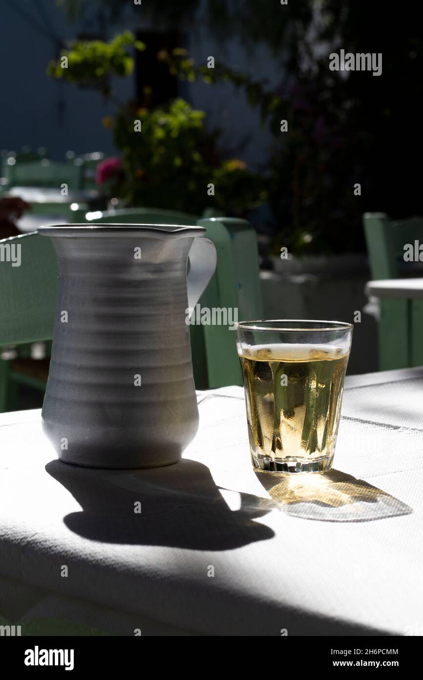 Bicchiere di vino con caraffa, isola di Folegandros, Grecia. Semplice bevanda greca, tipicamente servita in una taverna. Vista ravvicinata, scatto verticale con selezione fo Foto Stock