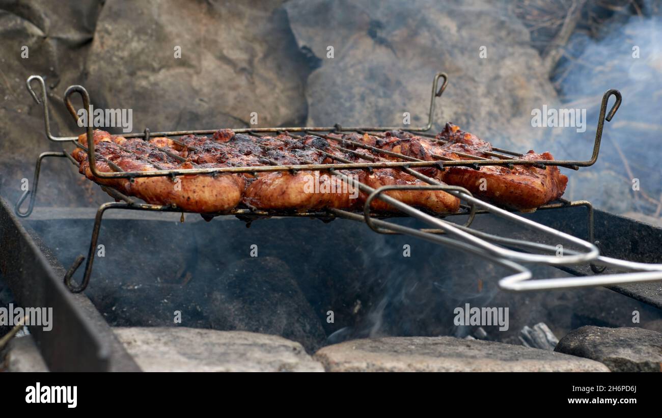 Grigliare le ali di pollo sulla griglia del barbecue con fiamme e fumo. Messa a fuoco selettiva. Cibo estivo. Idee per barbecue, grigliate, barbecue. Foto Stock