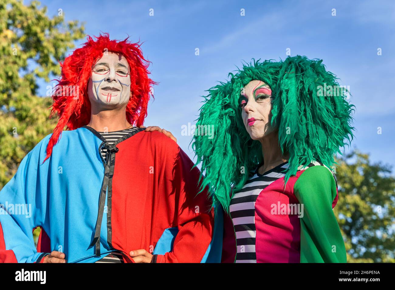 Positivo harlequins maschio e femmina con facce dipinte in costumi colorati e parrucche sorridenti in una giornata di sole. Foto Stock