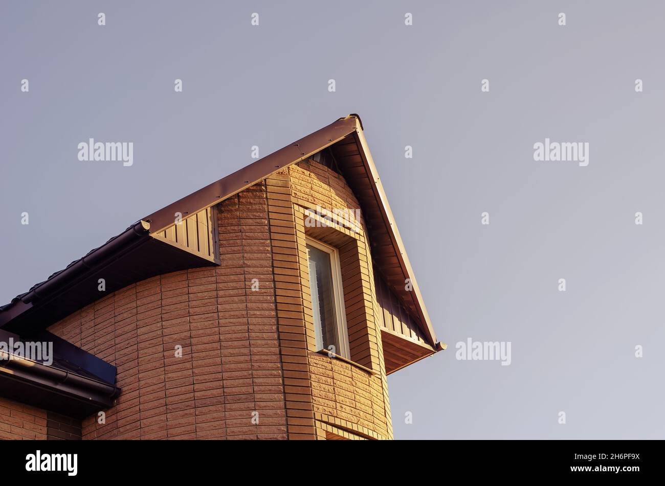 La cima di una bella villa moderna in pietra contro un cielo senza nuvole. La casa è fiancheggiata da piastrelle gialle. Tetto marrone con protezioni da neve. Es. Reali e moderni Foto Stock