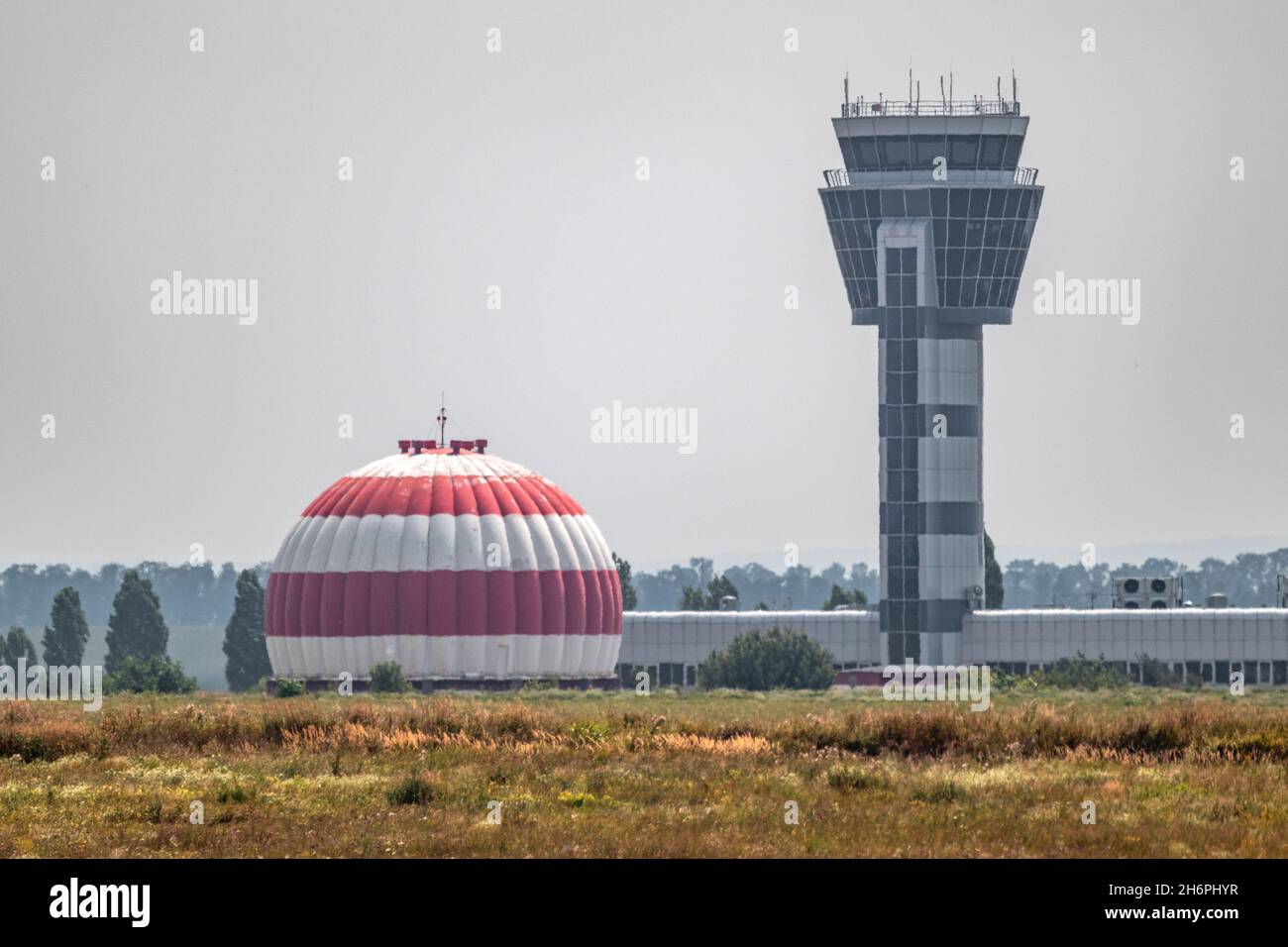 Torre di controllo dell'aeroporto internazionale e radome o edificio a cupola radar dell'aviazione dipinto in strisce rosse e bianche in campo di erba secca con cielo grigio. Khar Foto Stock