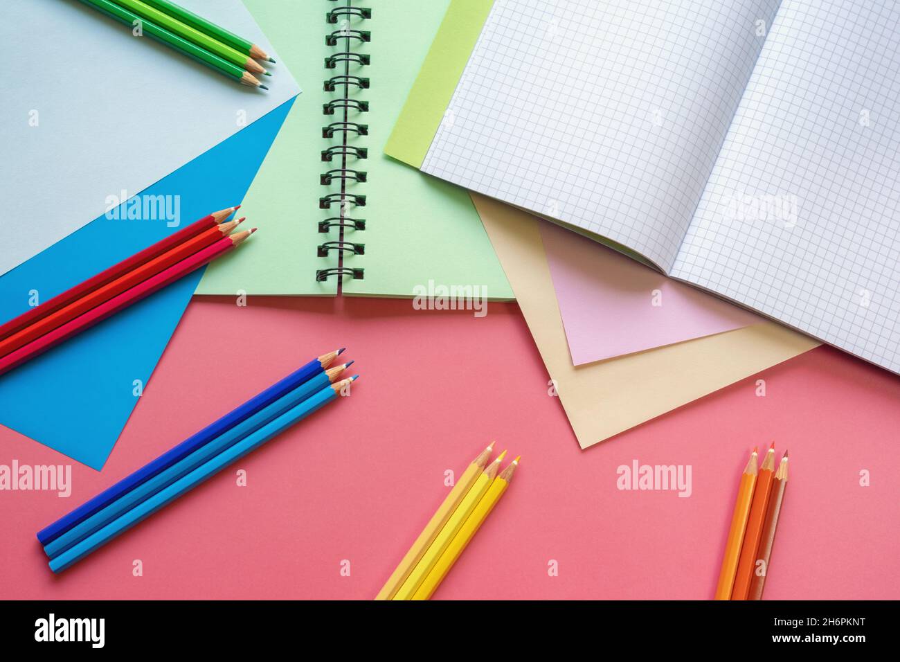 Concetti di scuola e hobby. Fogli di carta colorati, matite colorate e notebook su sfondo di carta rosa. Spazio di copia Foto Stock