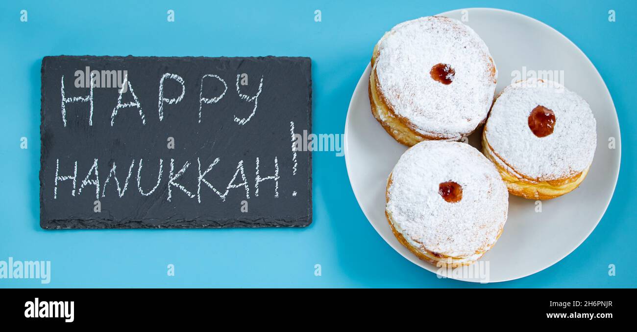 Felice Hanukkah. Dessert ebraico sufganiyot ciambelle su sfondo blu. Simbolo di festa religiosa giudaismo. Iscrizione sul bordo del gesso. Foto Stock