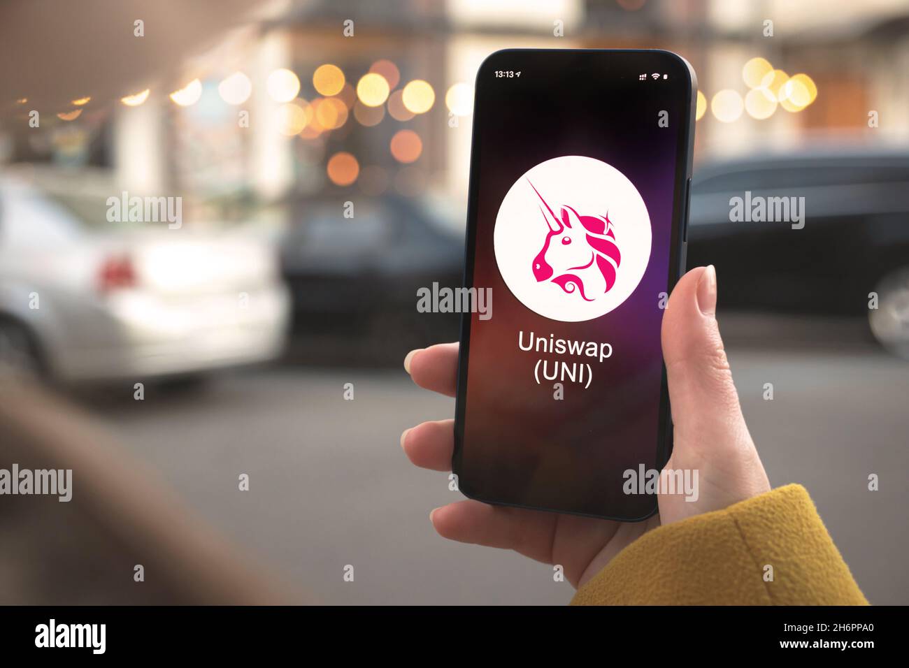 Simbolo di criptovaluta Uniswap UNI, logo. Concetto commerciale e finanziario. Mano con smartphone, schermo con icona di crittografia primo piano Foto Stock