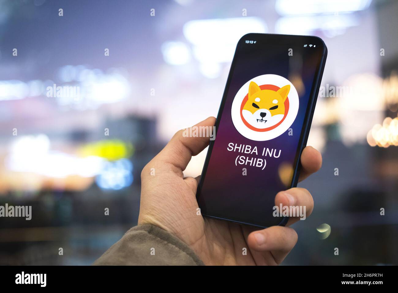 SIMBOLO di criptovaluta SHIBA INU, logo. Concetto commerciale e finanziario. Mano con smartphone, schermo con icona di crittografia primo piano Foto Stock