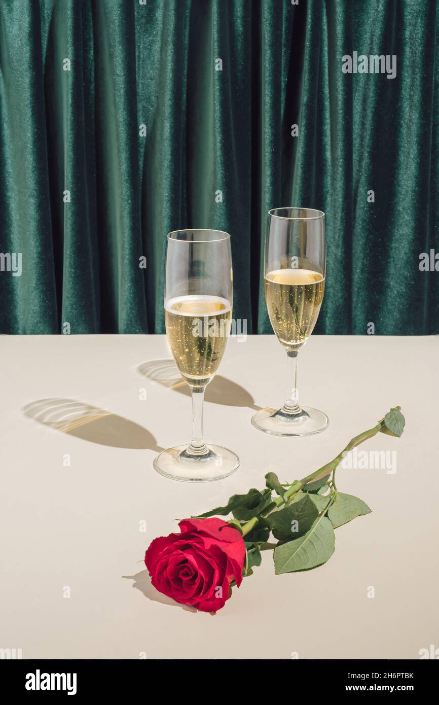Composizione minimale romantica di Capodanno 2022 o festa di Natale. Direzione artistica creativa d'epoca con bicchieri da champagne e rosa rossa. Foto Stock