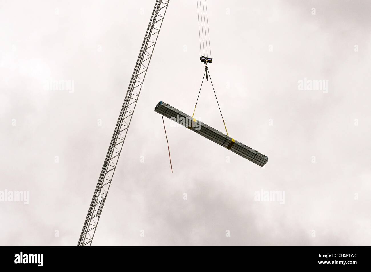 Carico di materiali da costruzione in acciaio che viene sollevato da una gru a torre sulla parte superiore di un nuovo edificio in costruzione Foto Stock