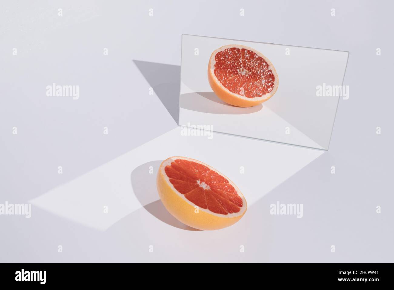 Composizione alla moda e minimal fatta di pompelmo rosso e il suo riflesso specchio su elegante sfondo bianco. Creativo concetto di frutta estiva. Foto Stock