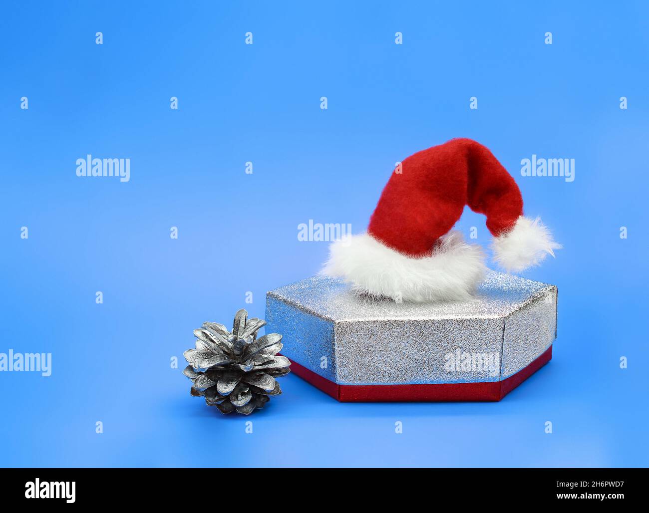 Scatola regalo in argento con cappello Babbo Natale e cono di pino su sfondo blu. Natale, Capodanno. Spazio di copia Foto Stock