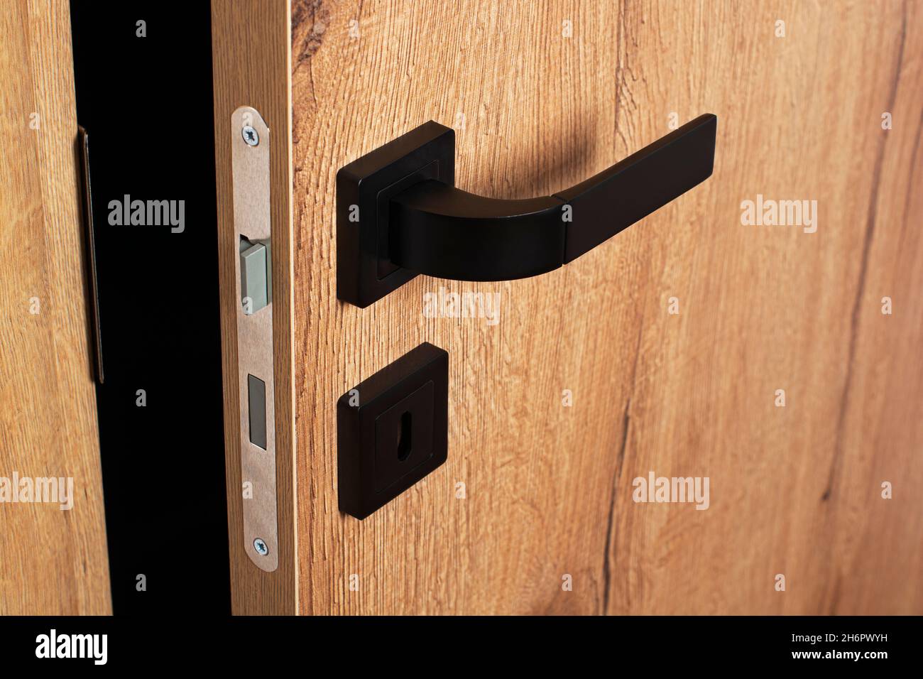 Primo piano porta parzialmente aperta. Porta in legno con maniglia nera Foto Stock