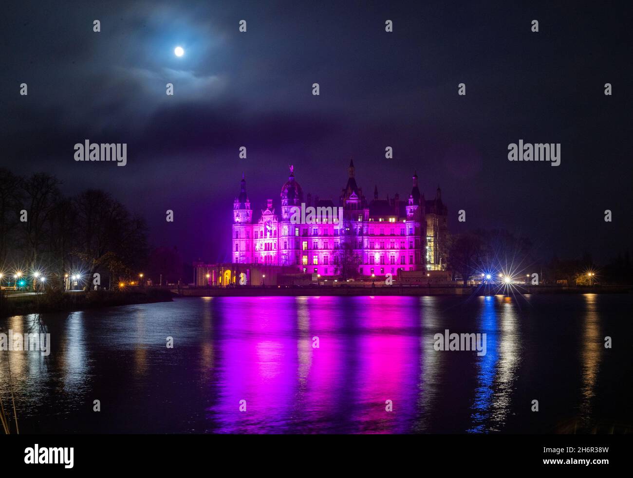 Schwerin, Germania. 17 novembre 2021. La luna brilla sul Castello di Schwerin, illuminato con luce viola nella Giornata Mondiale della prematurità. (Esposizione lunga) il 17 novembre, la Giornata prematura Mondiale del Bambino ci ricorda le grandi sfide che le famiglie con i bambini prematuri vanno attraverso. Credit: Jens Büttner/dpa-Zentralbild/dpa/Alamy Live News Foto Stock