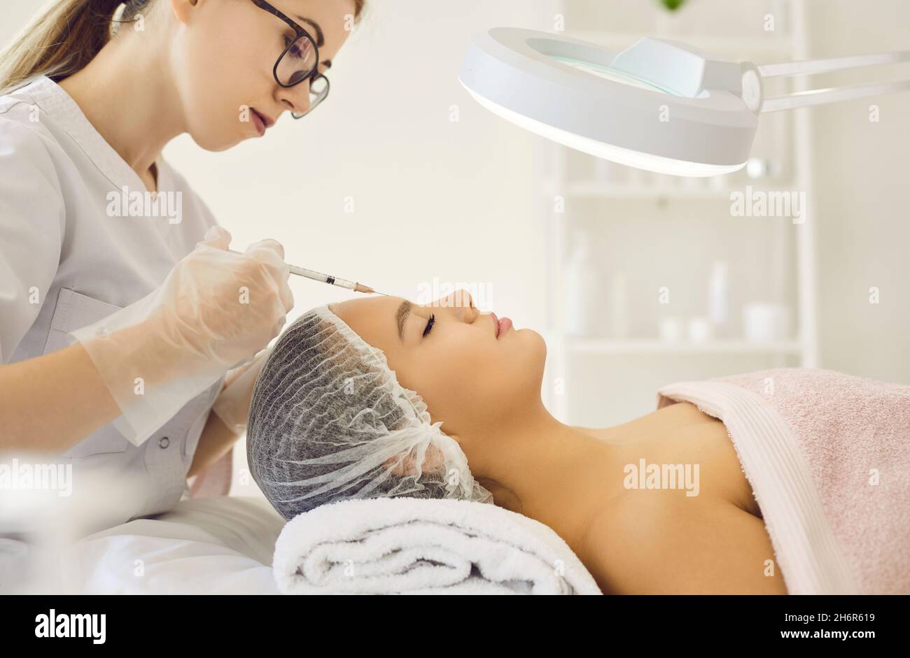 Beautician fa l'iniezione cosmetica fra le sopracciglia sulla faccia della donna bella. Foto Stock