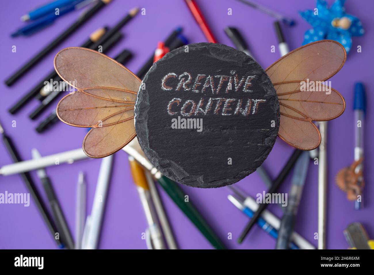 contenuto creativo scritto su una piastrella di pietra con ali di libellula circondate da un sacco di matite e penne Foto Stock