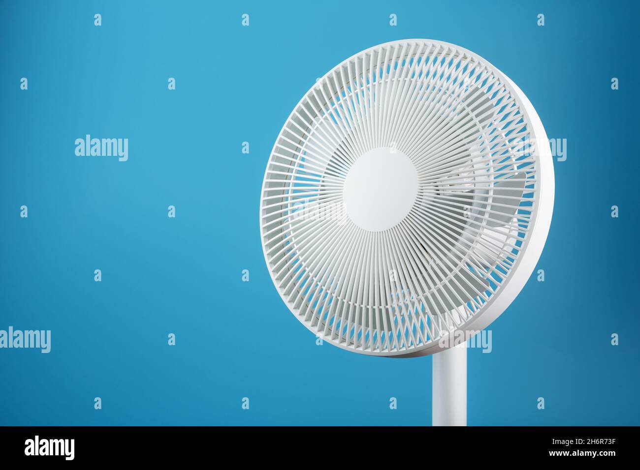 Moderno ventilatore elettrico bianco per raffreddare la stanza su sfondo blu. Spazio libero, stile minimalista. Foto Stock