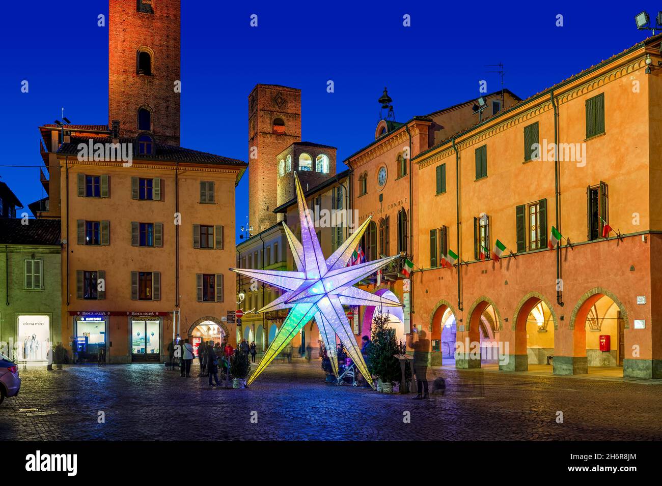 Installazione illuminata a forma di stella sulla piazza centrale tra edifici storici e torri medievali di Alba, Italia. Foto Stock