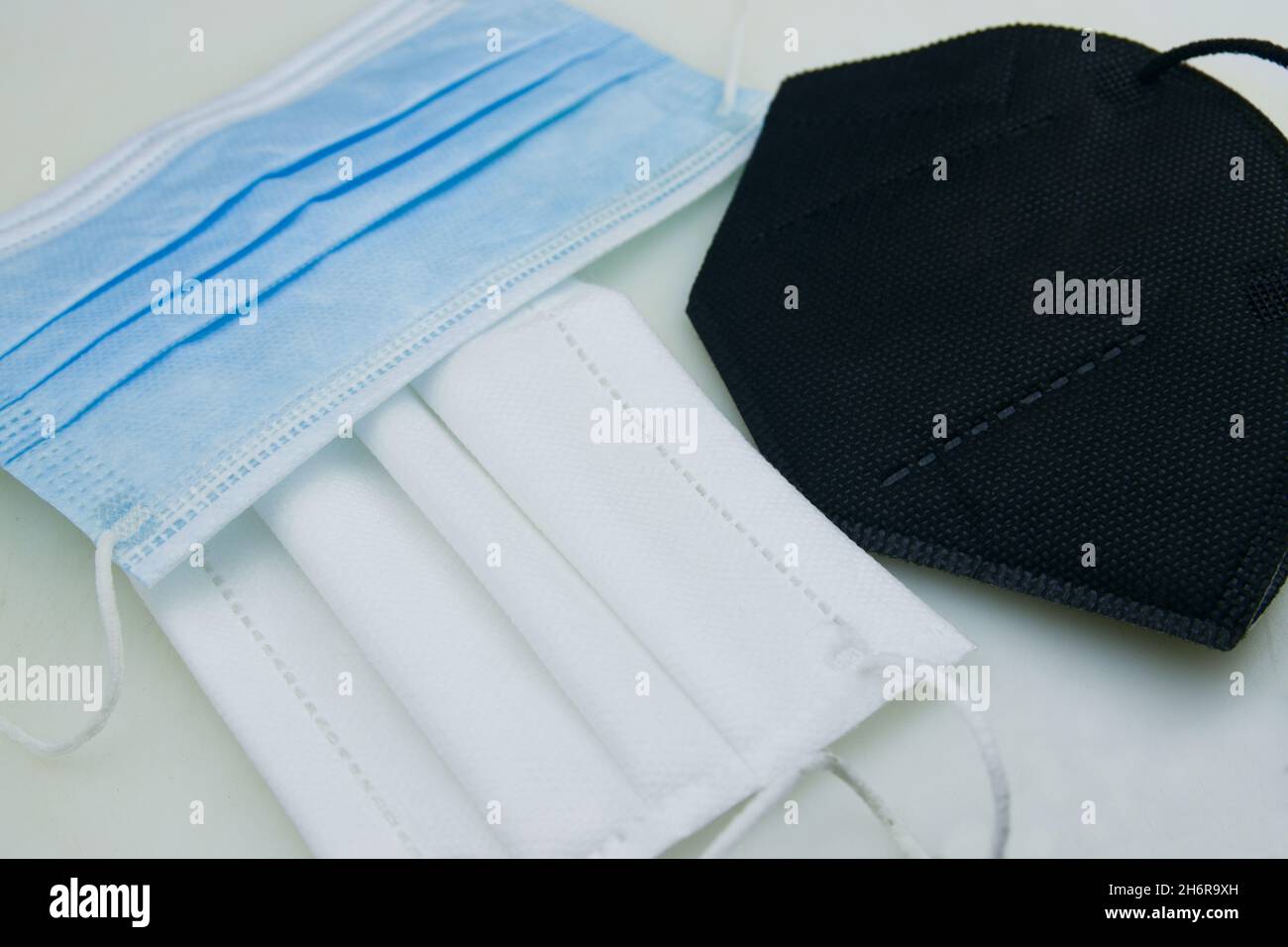 Confronto di vari tipi di maschere, la maschera igienica (blu), una maschera a tre strati (bianca) e una maschera FFP2 (nera) su un tavolo Foto Stock