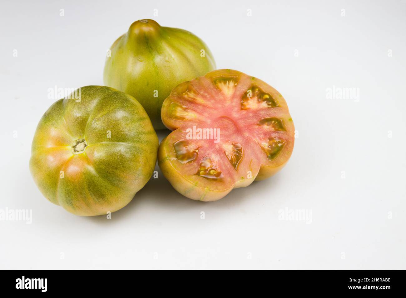 Primo piano di tre pomodori valenciani verdi della variante dello zio, uno dei quali tagliato a metà, su sfondo bianco Foto Stock