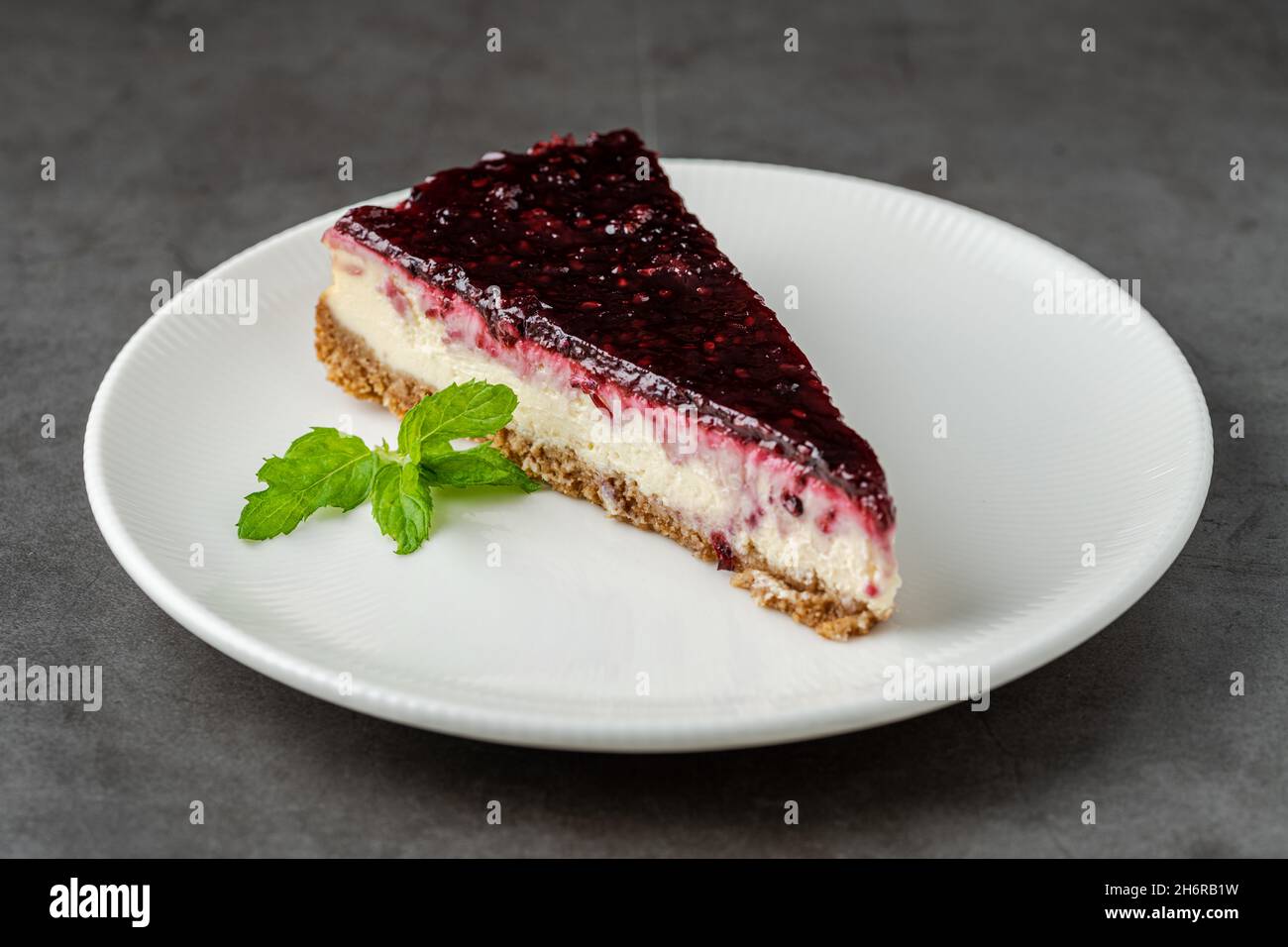 Cheesecake al lampone su piastra bianca su tavola di pietra scura Foto Stock